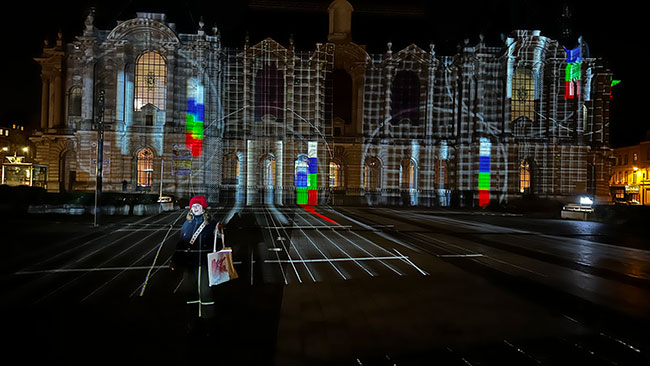 A women poses in front of a large building that is illuminated with a projector test pattern.
