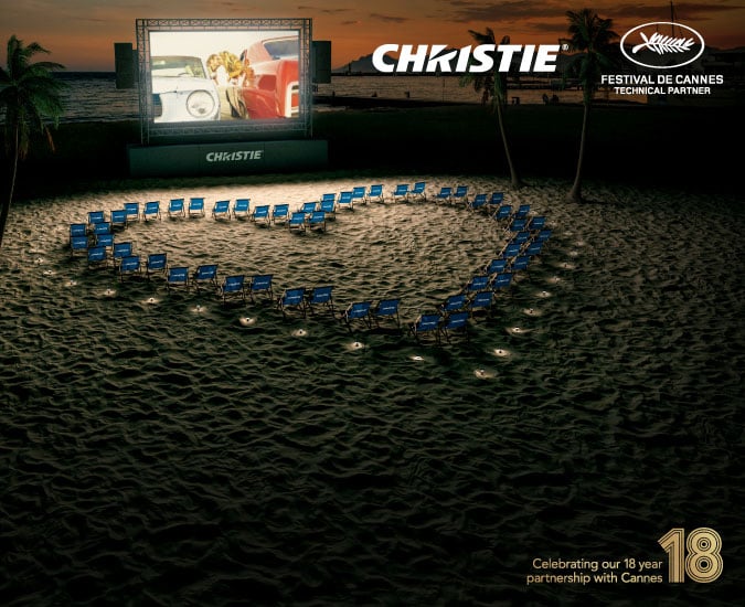Christie branded blue beach chairs placed in a heart shape on a beach in front of a movie screen
