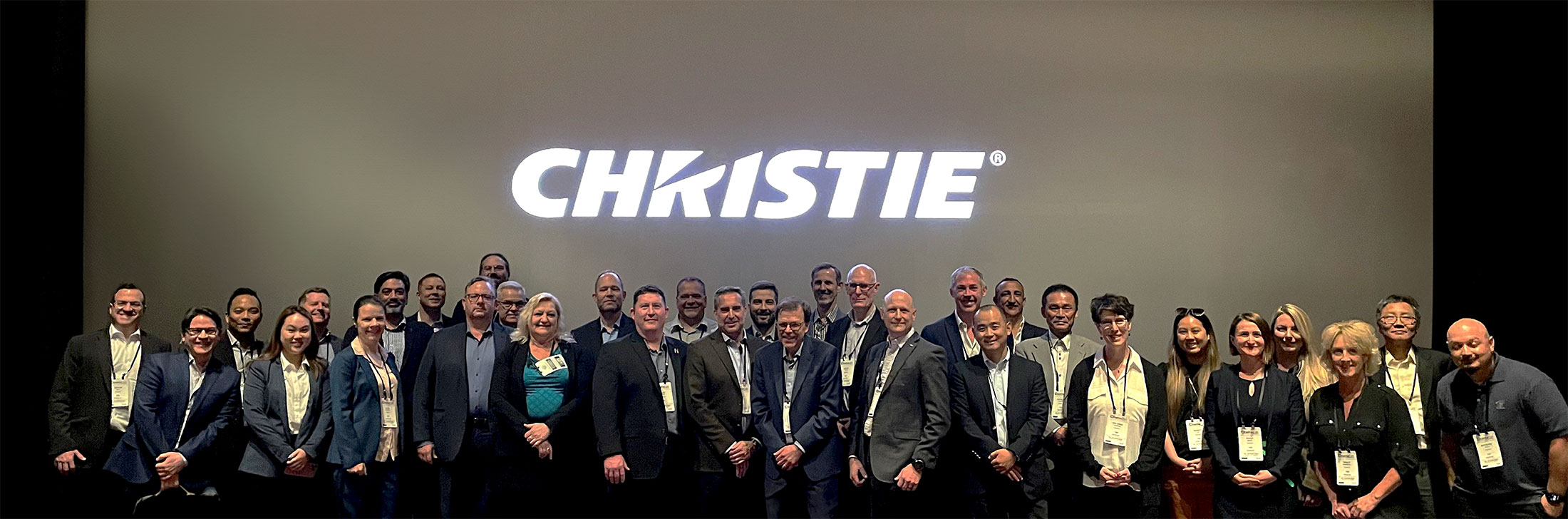 A group photo of the Christie Cinema team standing in front of a movie screen displaying the Christie logo