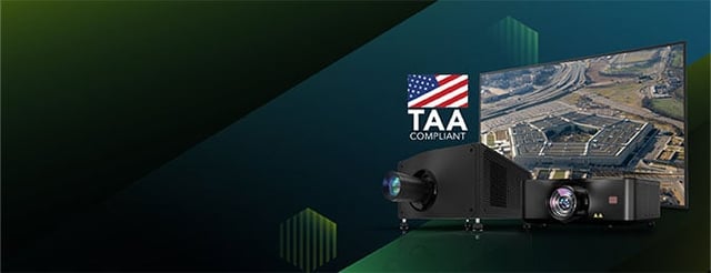 A man in fatigues standing in front of seated group of people, gesturing to an image on a large screen, with the TAA compliant logo