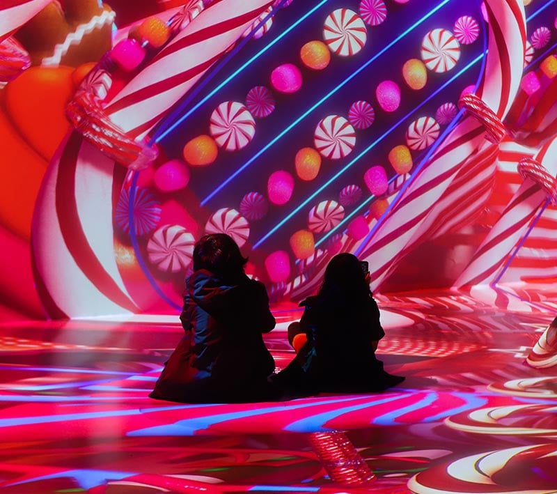 Two people sitting in front of images of candy projected onto a wall with a 4k projector