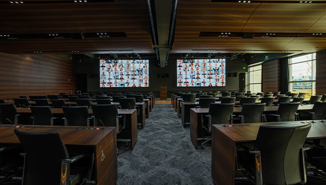 Conference desks and chairs facing two LED video walls at the front of the room. 