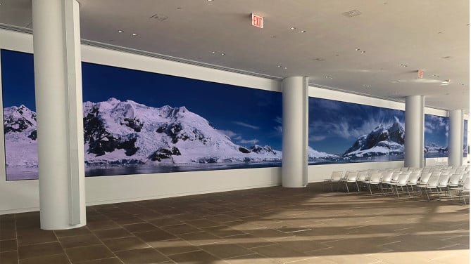 A large video wall featuring images of snowy mountains in an empty room with chairs in it. 