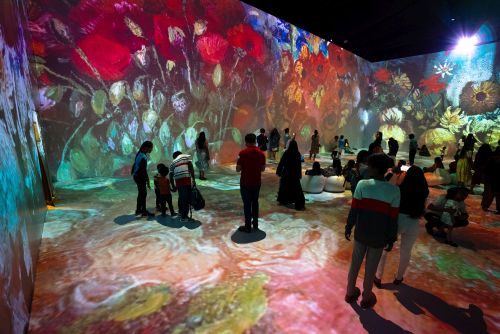 People in a room with a red flower painting projected onto the walls, creating an immersive experience.