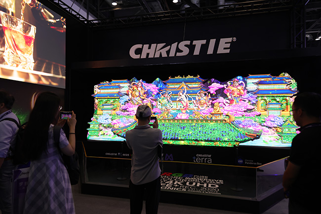 A man and a woman are standing in front of a projection mapped 3D wall taking pictures.