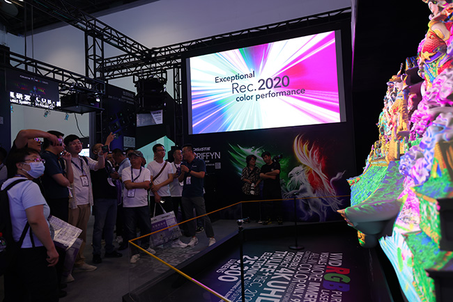 People standing in front of the 3D wall on the left with the wall on the right. A screen with the text 'Exceptional Rec. 2020 color performance' hangs above in the middle. 