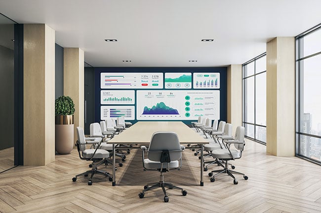 A meeting room with an LED video wall display at the end, and a large table surrounded by chairs.