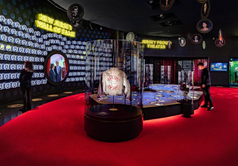 A museum exhibit with a jacket in a glass case and dynamic visuals on the walls.