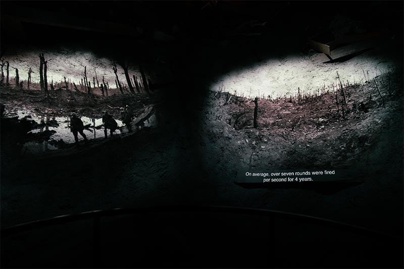Black and white images from a battlefield are projected onto a dark, textured wall.