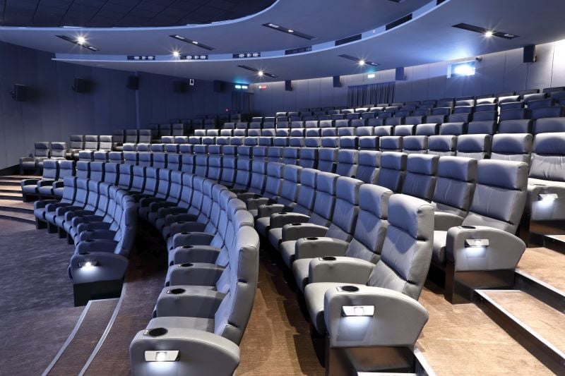 An empty movie theatre with grey stadium seating.