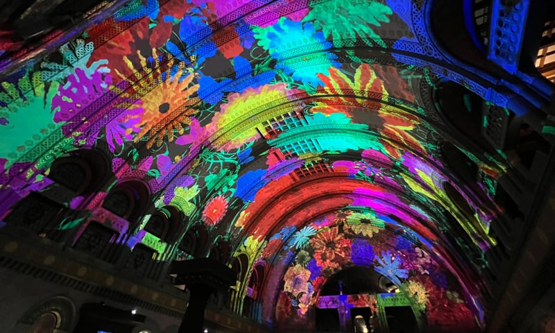 An ornate barrel-shaped ceiling is projection mapped with vivid images of flowers.