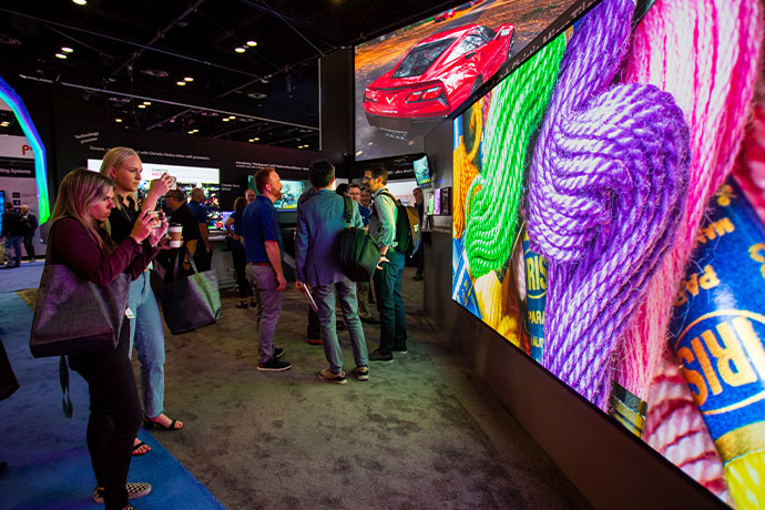 Two white people take a picture of a MicroTiles LED 0.75mm video wall with bright colored thread on it.