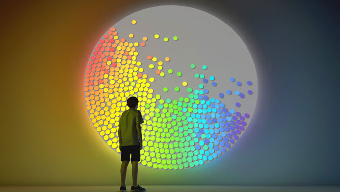 Child stands in front of projection of rainbow coloured circles.