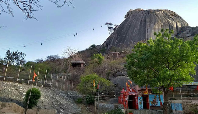 Image of a large hill that is formed out of rock with a tree in the foreground.
